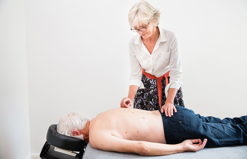 Sabine Vahling setzt Akupunkturnadeln auf dem Rücken eines Patienten